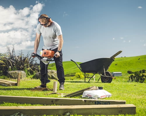 A man outside using a post borer to dig into the ground