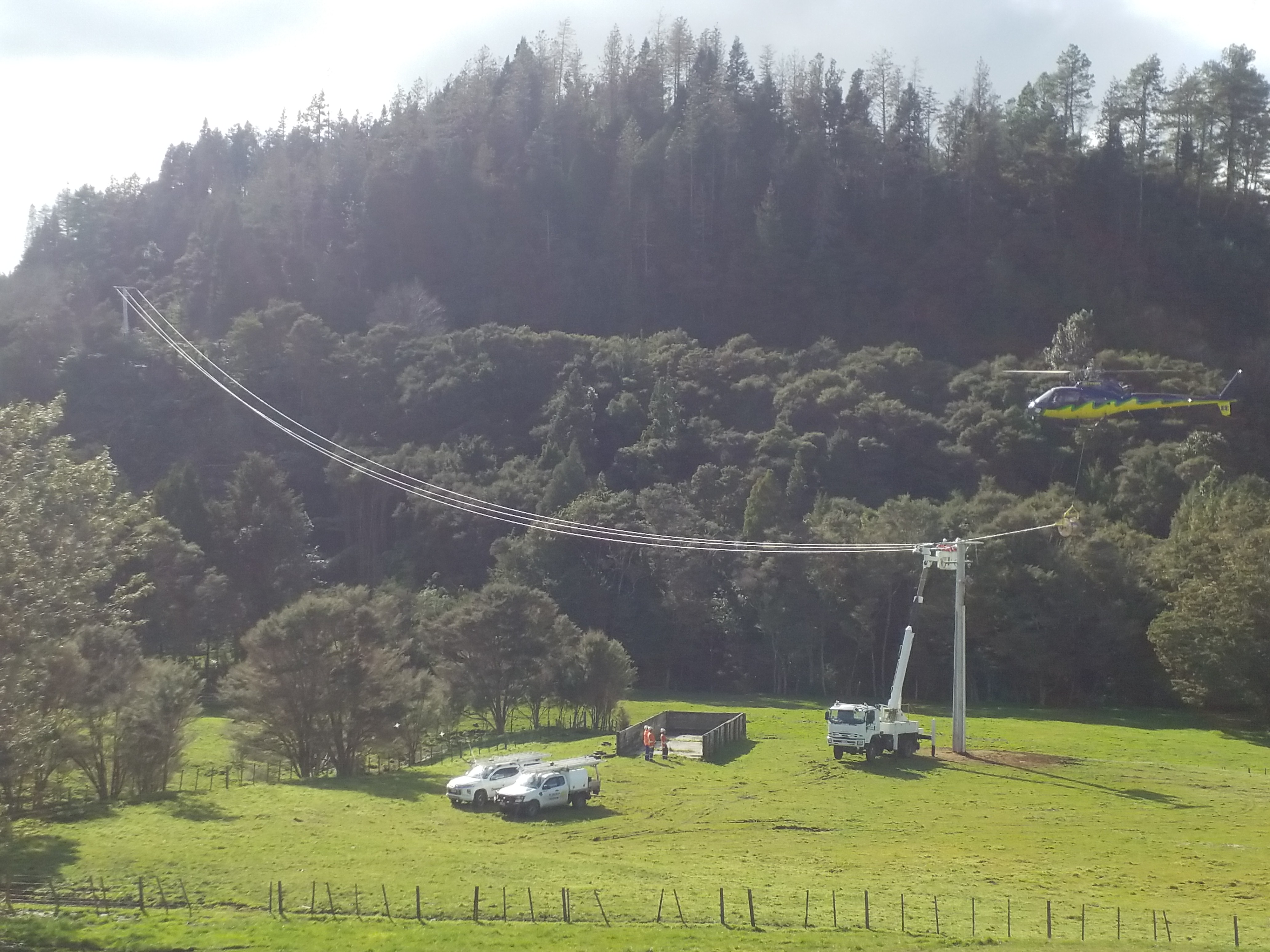A helicopter being used to string lines between two power poles in a rural setting