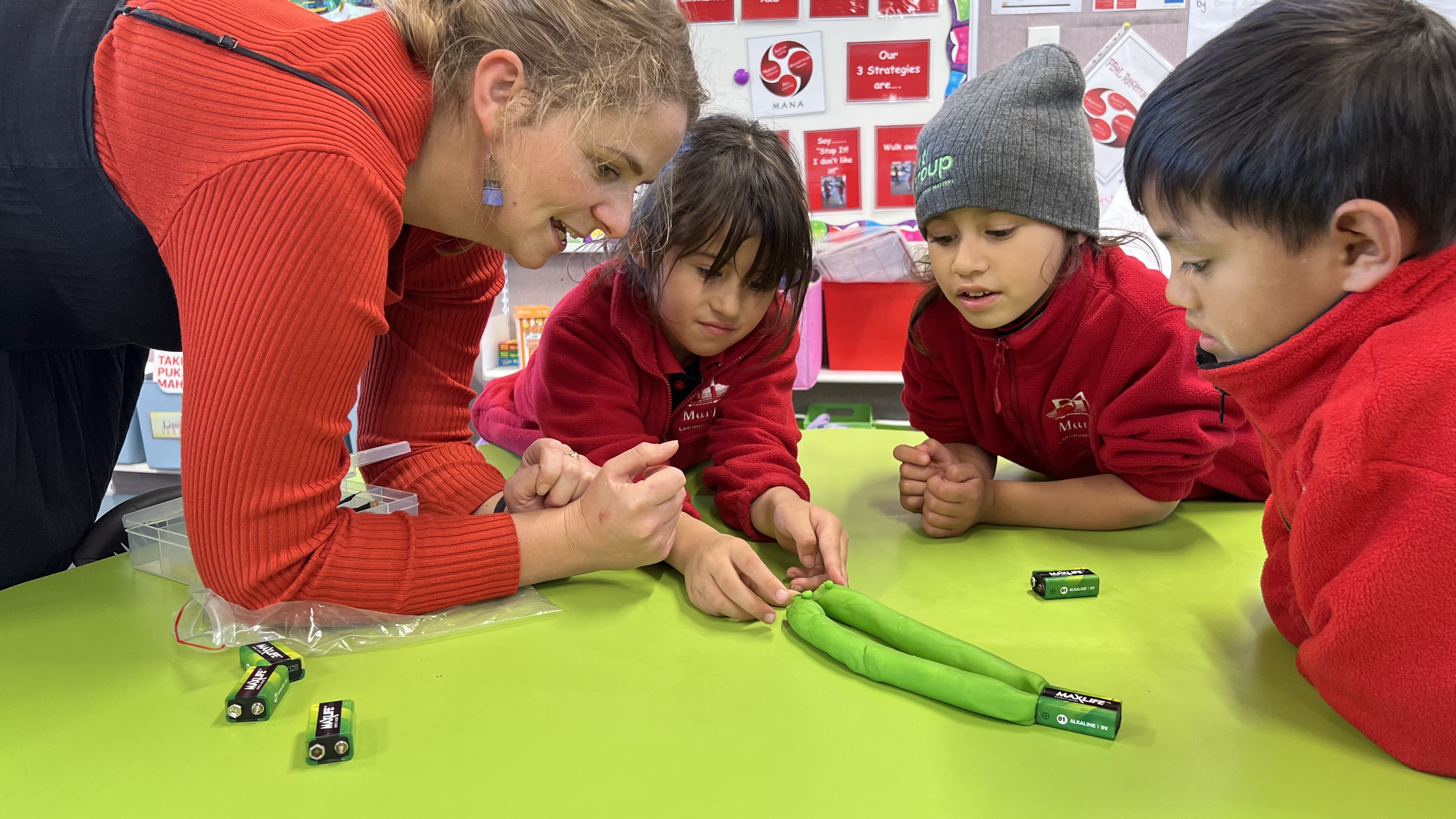 A teacher showing primary school students how to make an electricity circuit.