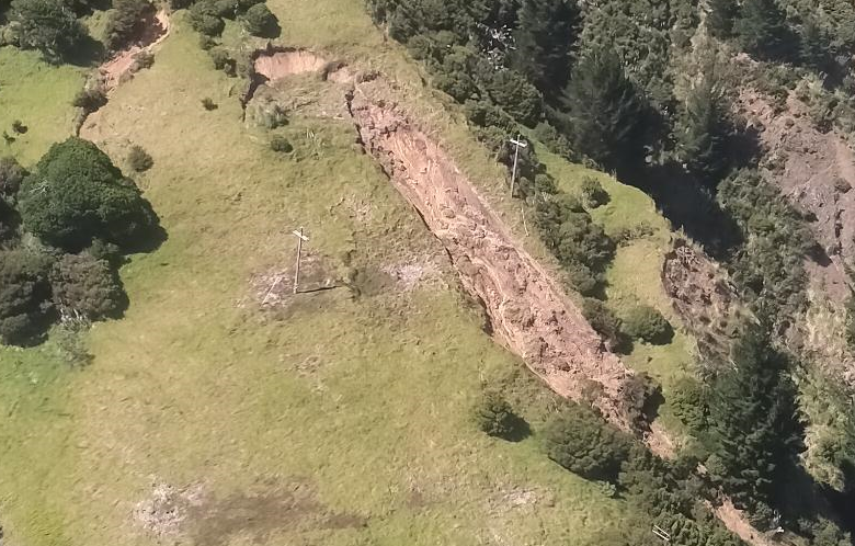 An aerial photo of rural land on a steep hillside with a large landslip going between two power poles