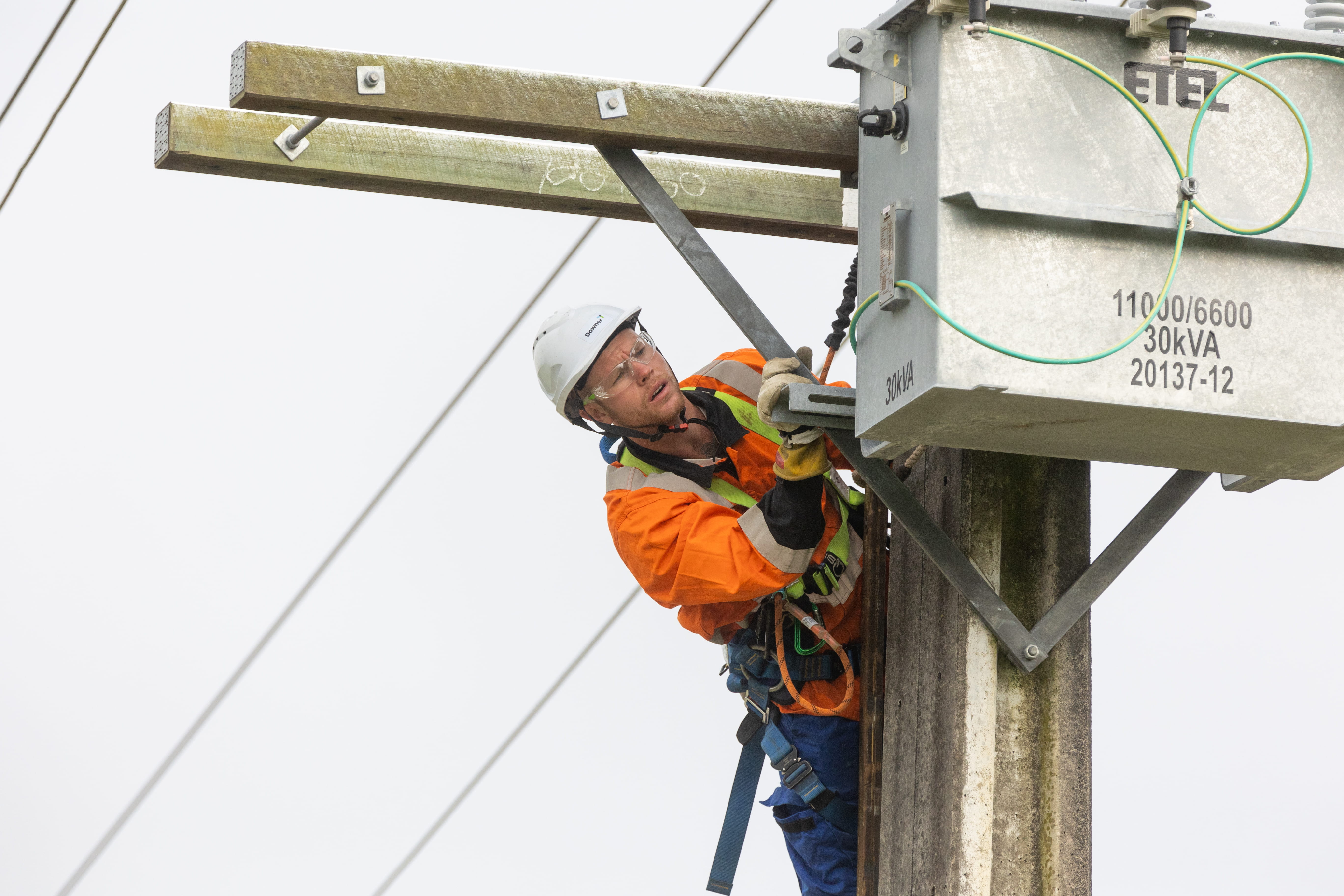 Electricity crewman up power pole working on a pole-mounted transformer.