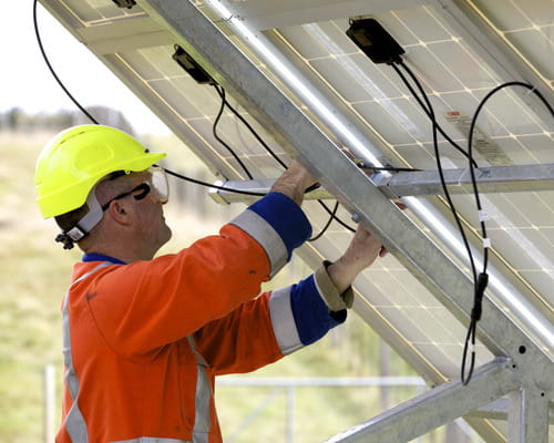 Worker in hi vis standing behind solar panel